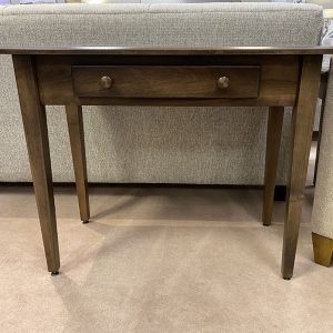 Wooden table with single drawer on carpet floor.