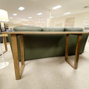 Wooden console table behind green leather couch in store.